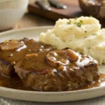 slow cooker cube steak with gravy, paired with creamy mashed potatoes on a white plate.